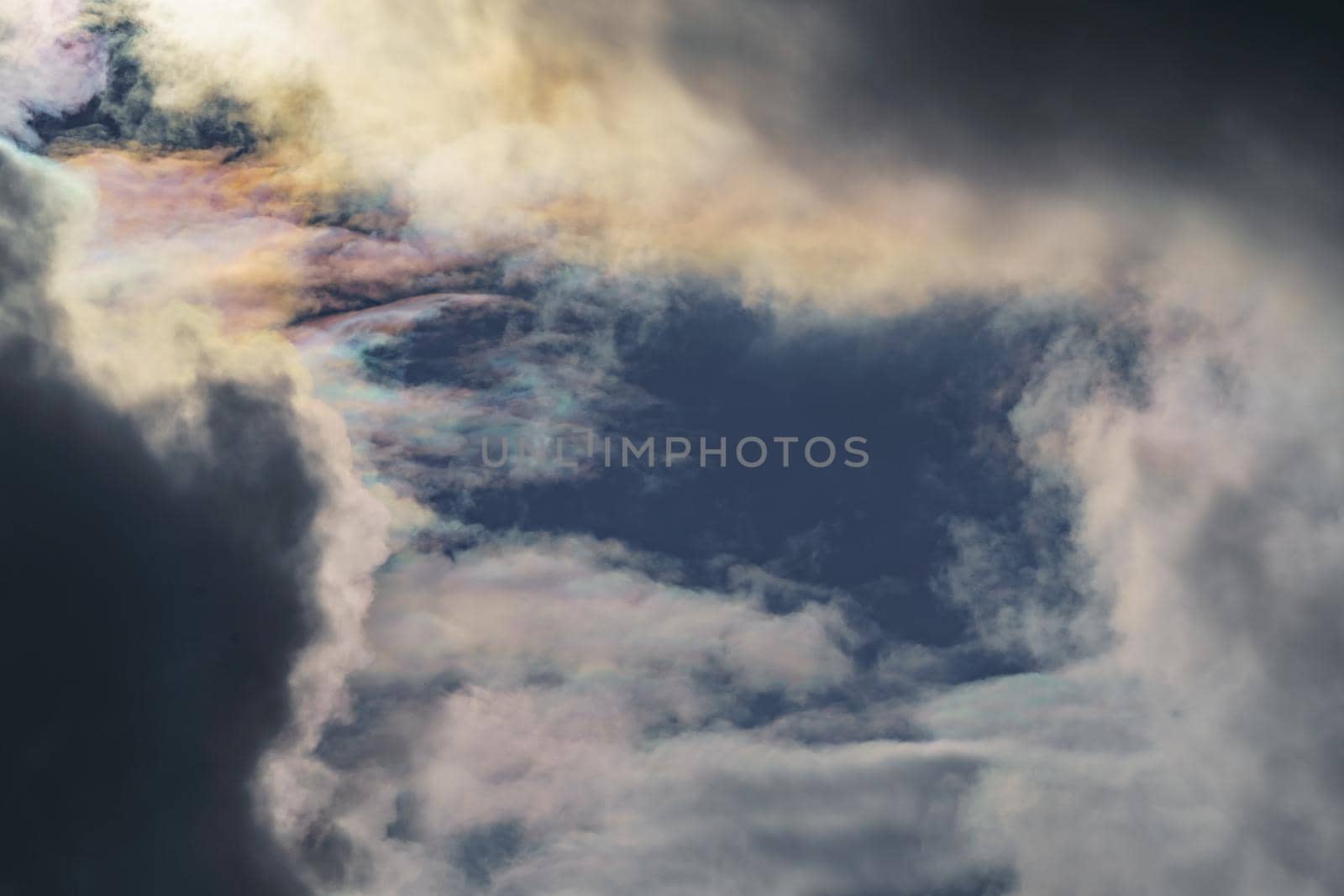 Diffraction of light on drops of supercooled water in clouds, rainbow clouds against the blue sky in clear sunny weather, irisation of cumulus clouds, optical phenomenon, spectral colors. High quality photo