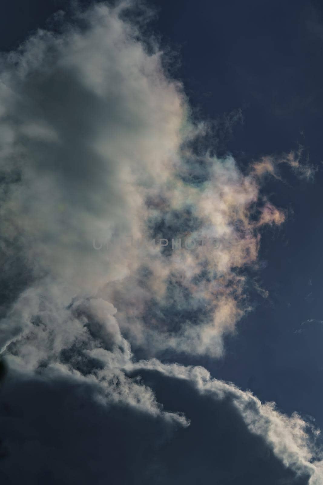 Diffraction of light on drops of supercooled water in clouds, rainbow clouds against the blue sky in clear sunny weather, irisation of cumulus clouds, optical phenomenon, spectral colors. High quality photo