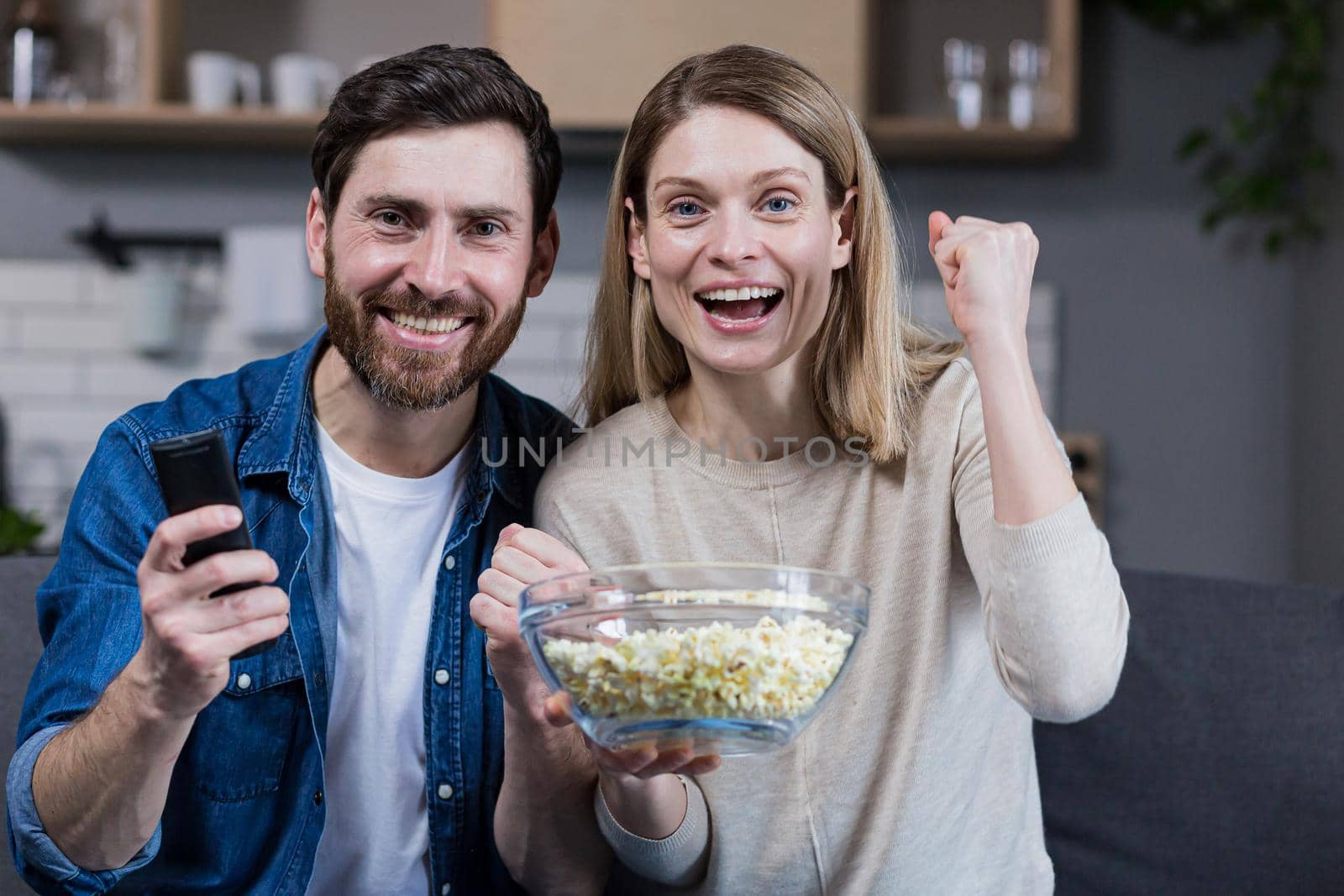 Photo of close couple man and woman together at home having fun and happily watching TV and eating popcorn