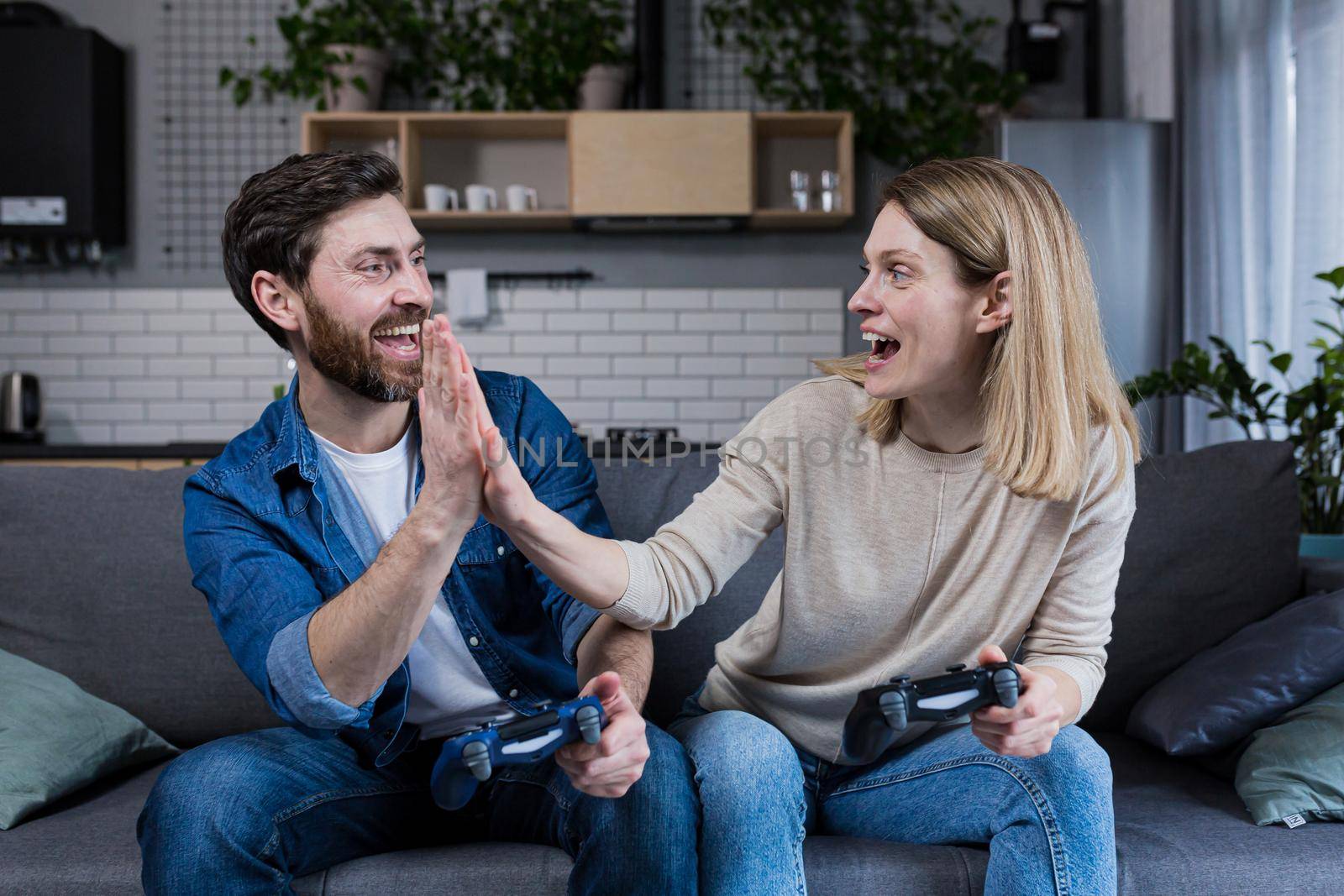 Happy couple man and woman playing game using joystick while sitting on sofa at home