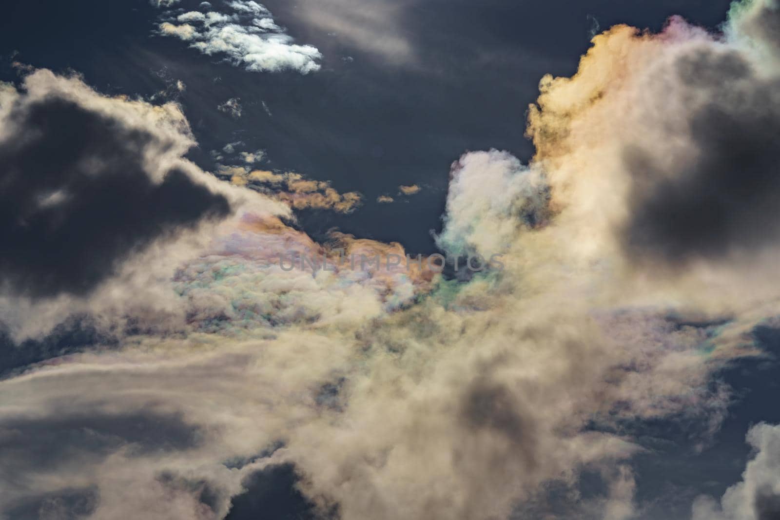 Diffraction of light on drops of supercooled water in clouds, rainbow clouds against the blue sky in clear sunny weather, irisation of cumulus clouds, optical phenomenon, spectral colors. High quality photo