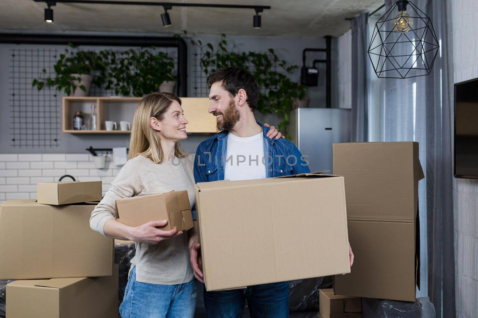 Happy couple man and woman live together, moved to a new rented apartment, holding cardboard boxes by voronaman