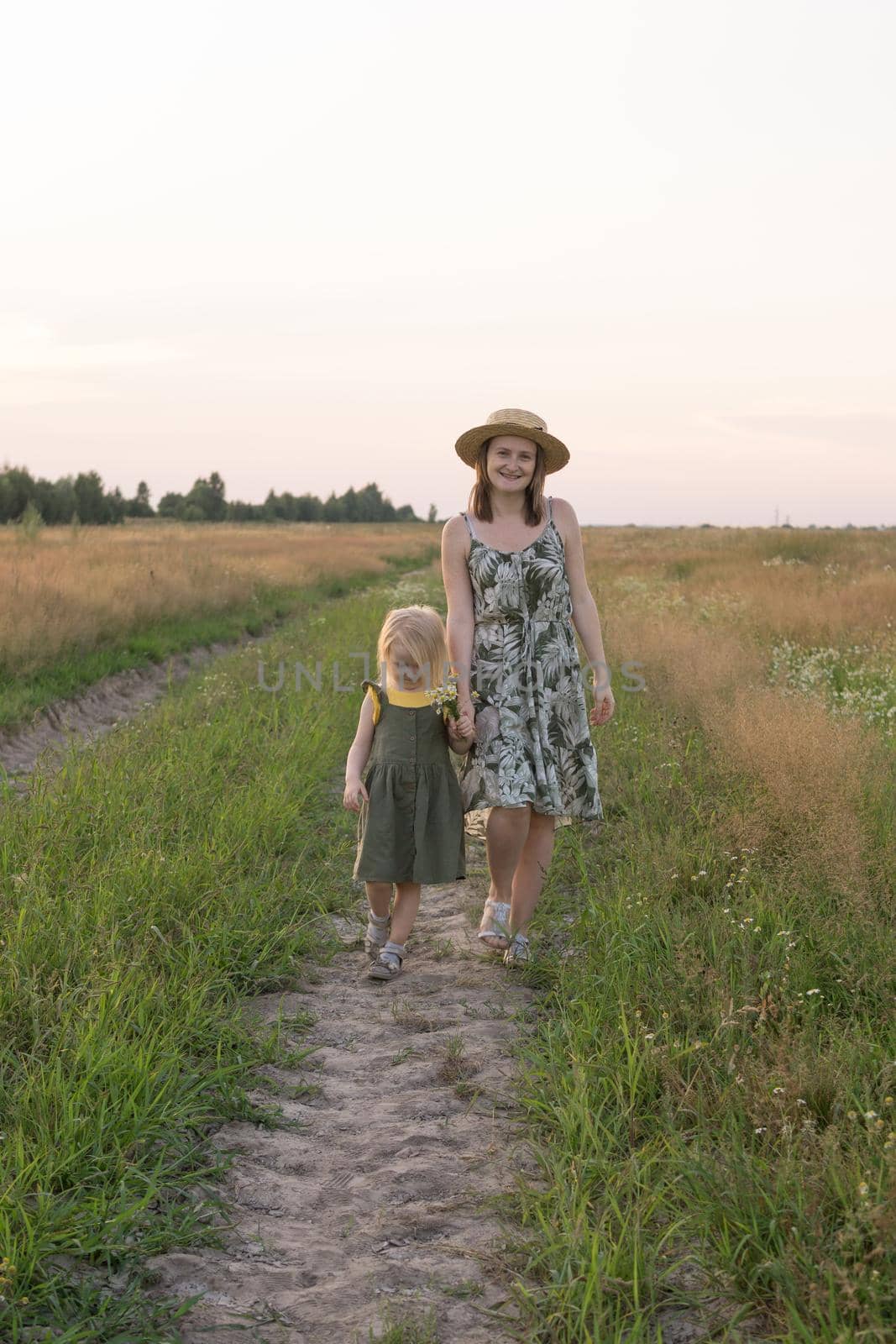 Mom and daughter walk through a chamomile field, and collect a bouquet of flowers. The concept of family relations, nature walks, freedom and a healthy lifestyle. by Annu1tochka