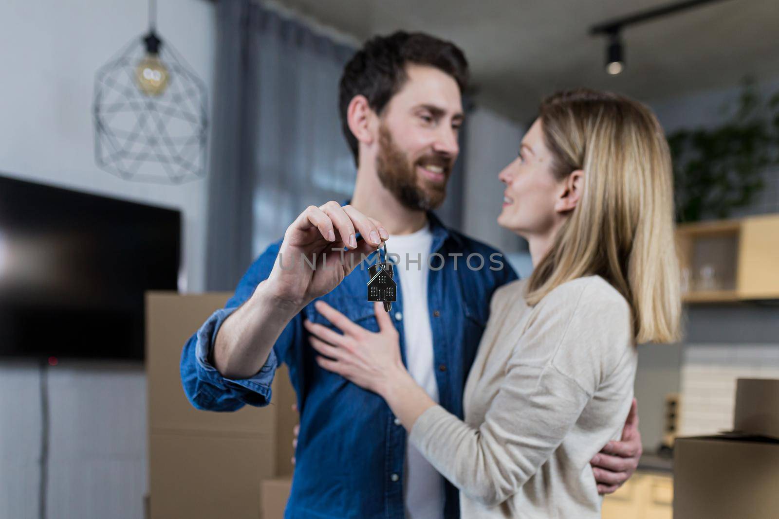 Selected focus, married couple man and woman happy together, hugging, holding the keys to their new apartment, housewarming, close-up photo