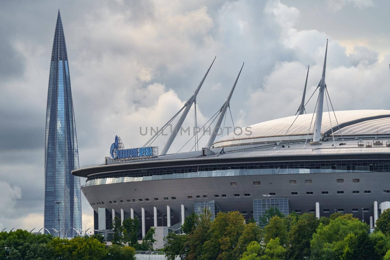 Russia, St. Petersburg, 29 July 2022: The new building of football stadium Gazprom Arena, the sliding metal roof glitters with spires in the sun, the skyscraper Lakhta for the gas company Gazprom. High quality photo