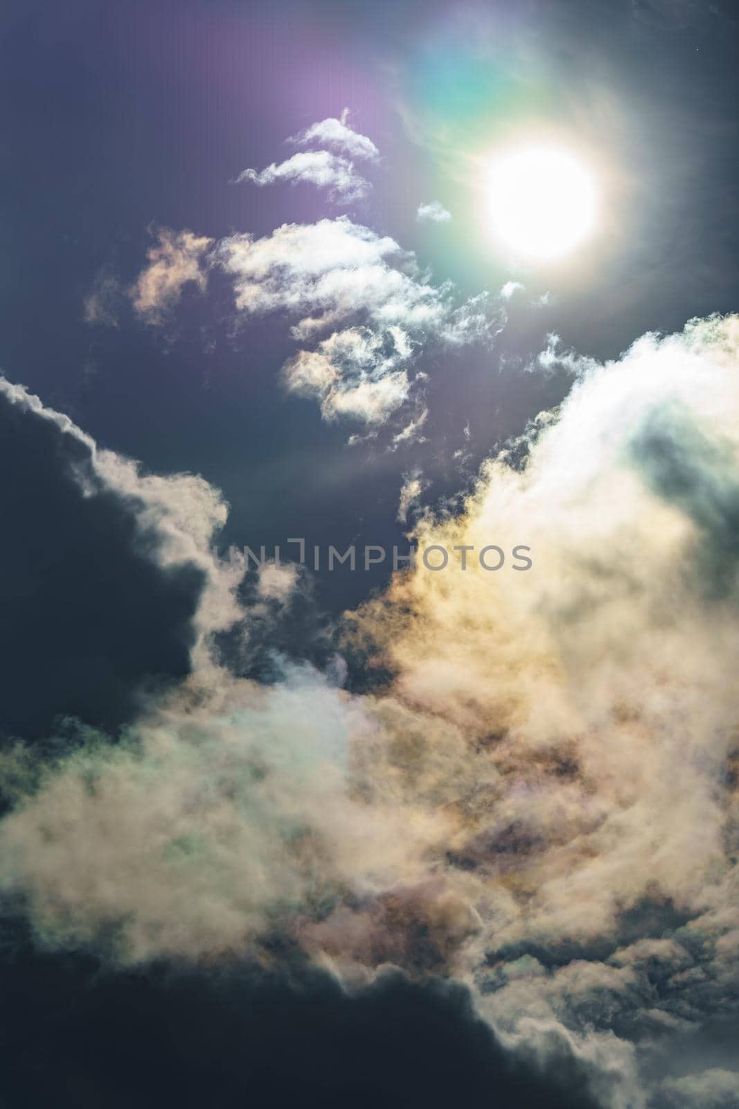 Diffraction of light on drops of supercooled water in clouds, rainbow clouds against the blue sky in clear sunny weather, irisation of cumulus clouds, optical phenomenon, spectral colors. High quality photo