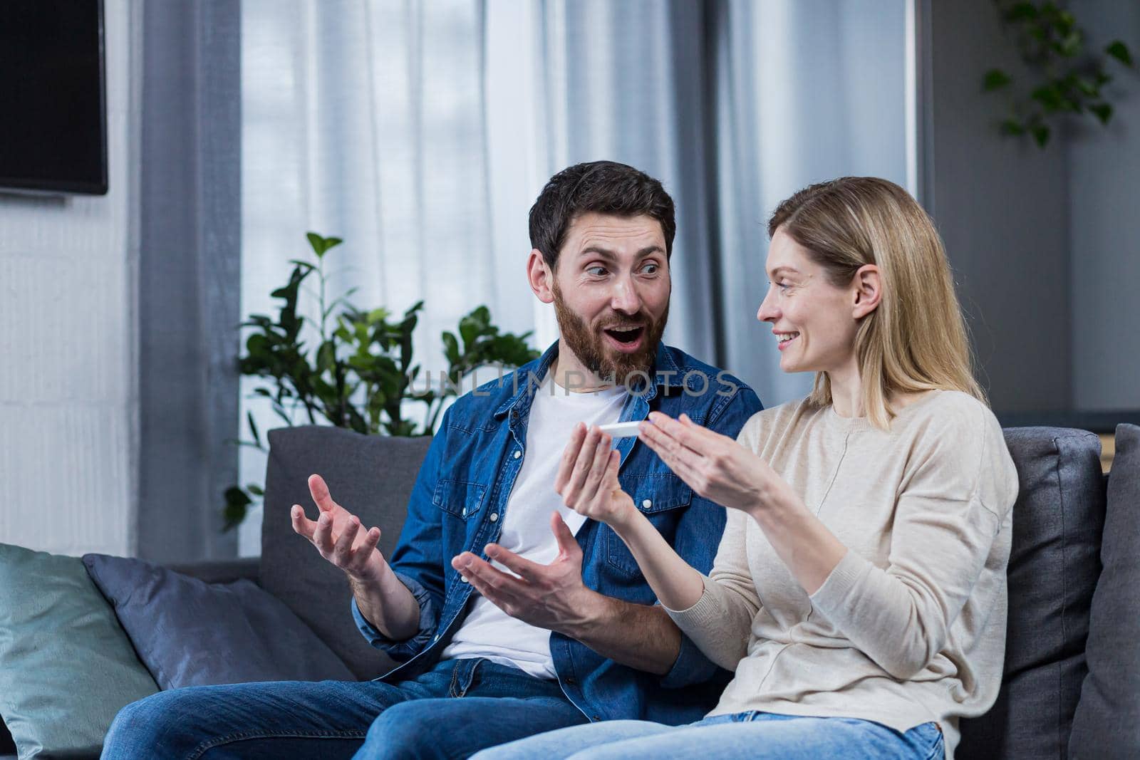 Happy couple man and woman on the couch sitting and rejoicing in a positive pregnancy test