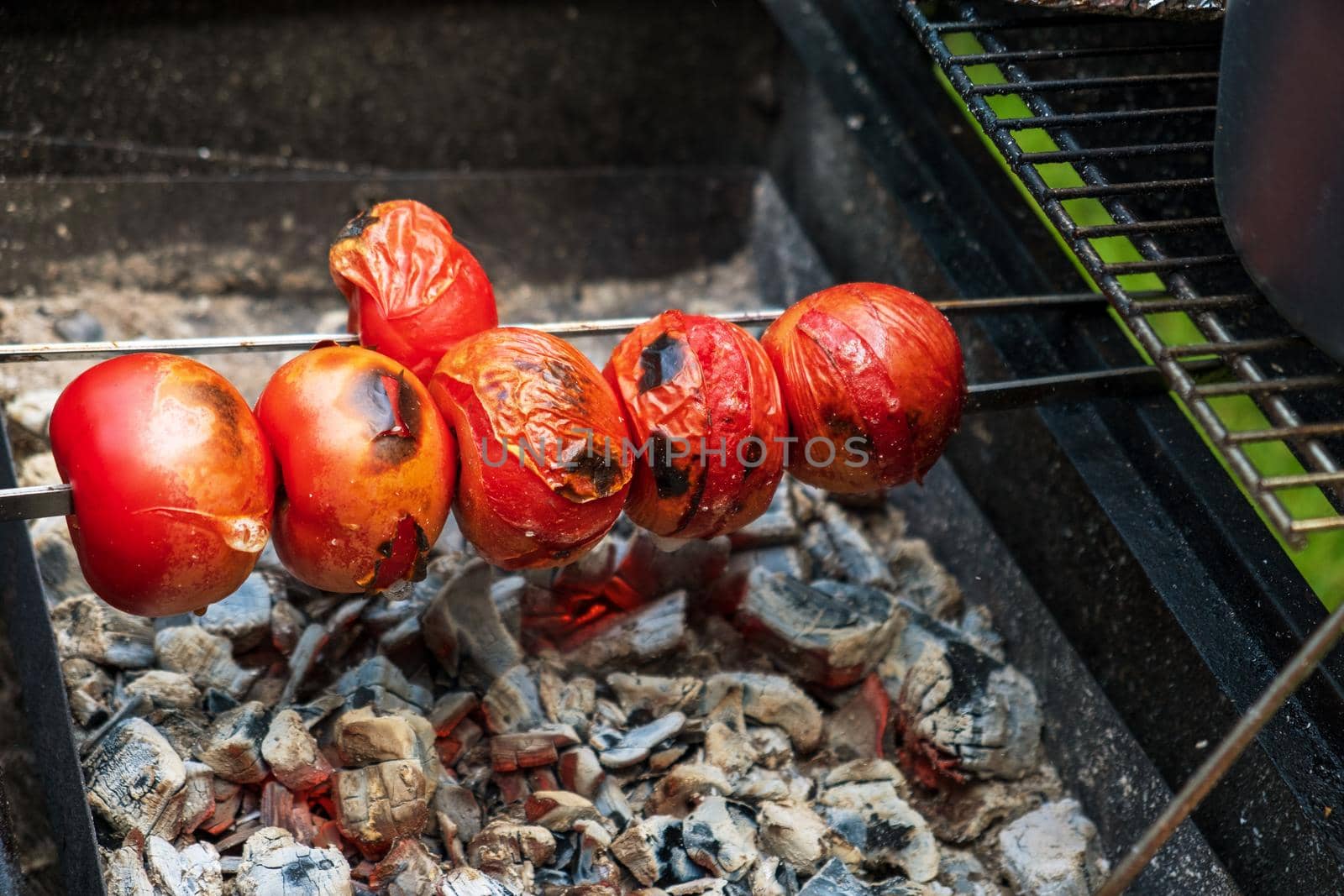 Ripe fresh tomatoes are grilled on a skewer over hot coals. Selective focus.