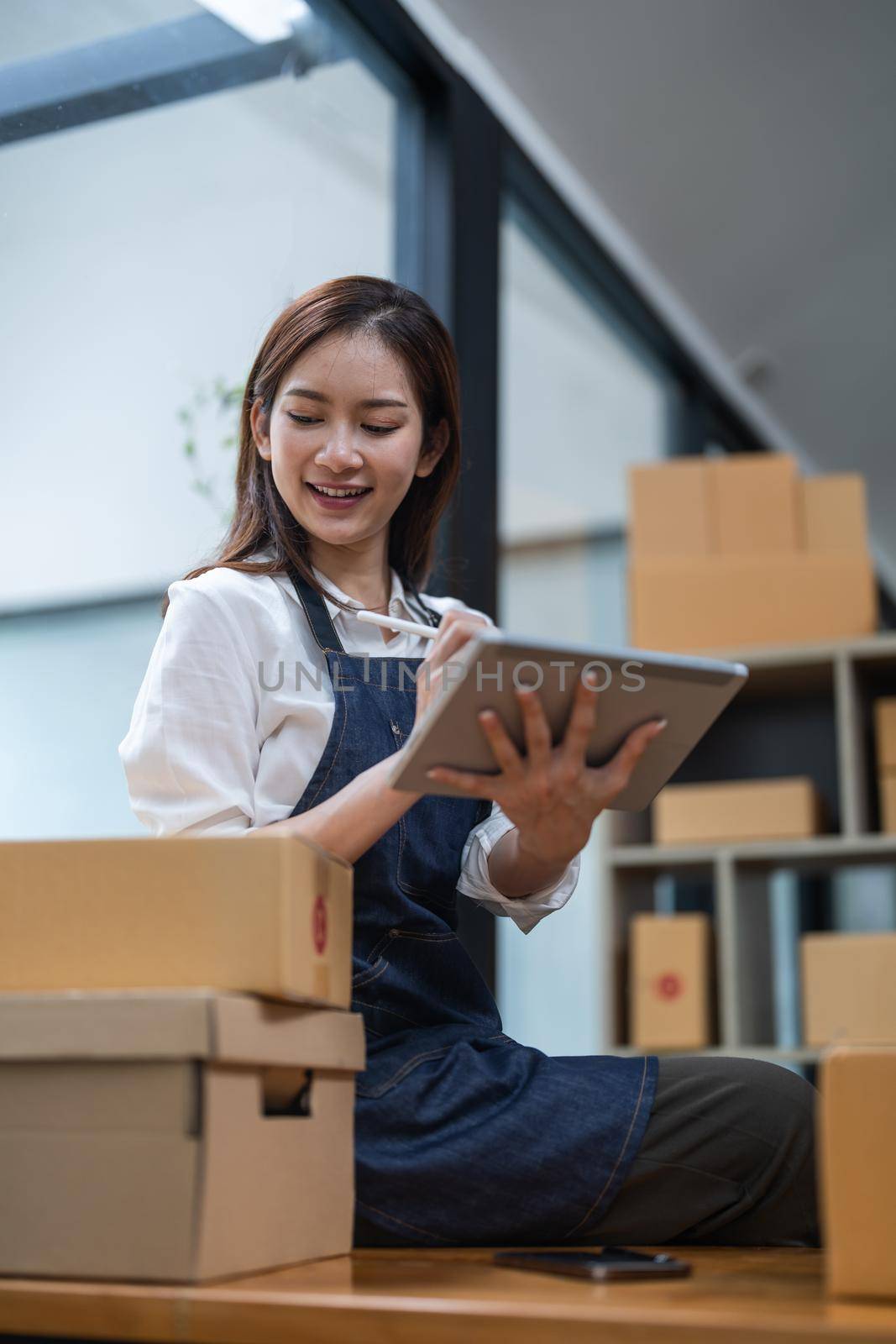 Asian female entrepreneur checking orders to arrange the produce before packing the products in the inner boxes with the customers. Freelance concepts.