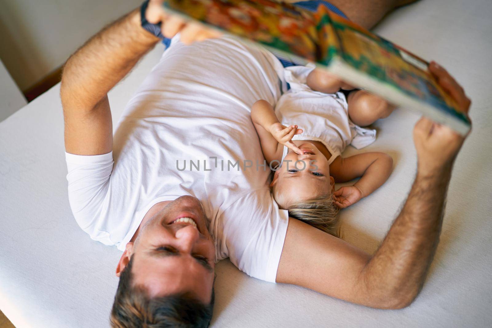 Dad reads a fairy-tale book to small daughter while lying on bed. High quality photo