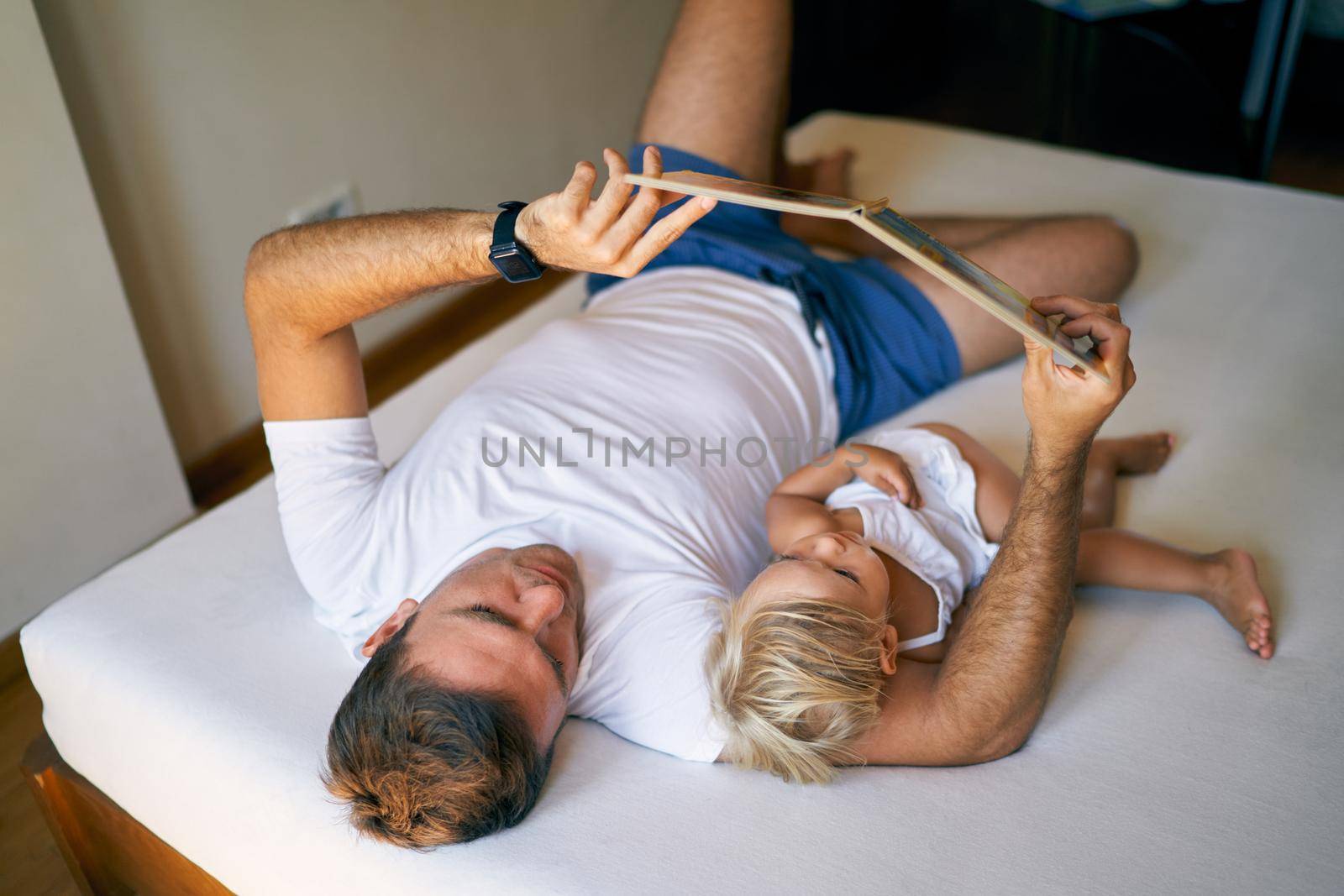 Dad and little girl reading a book lying on the bed. High quality photo