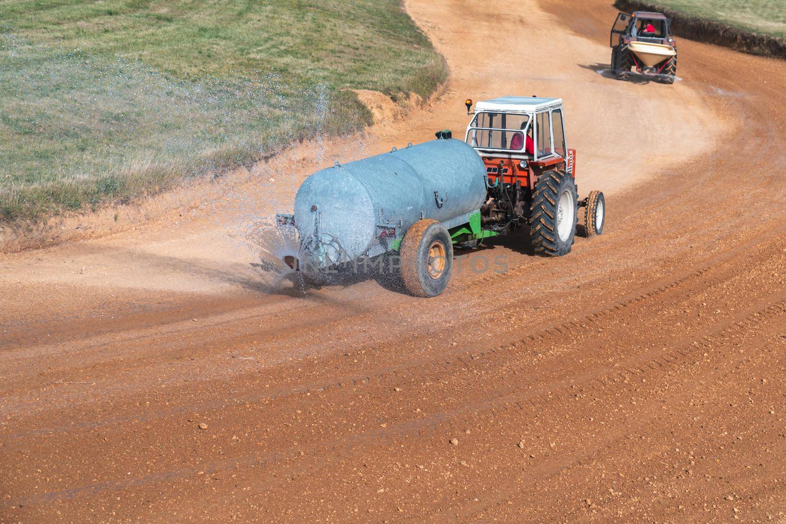 a tractor with a tank sprinkles water on the autocross track before the races.