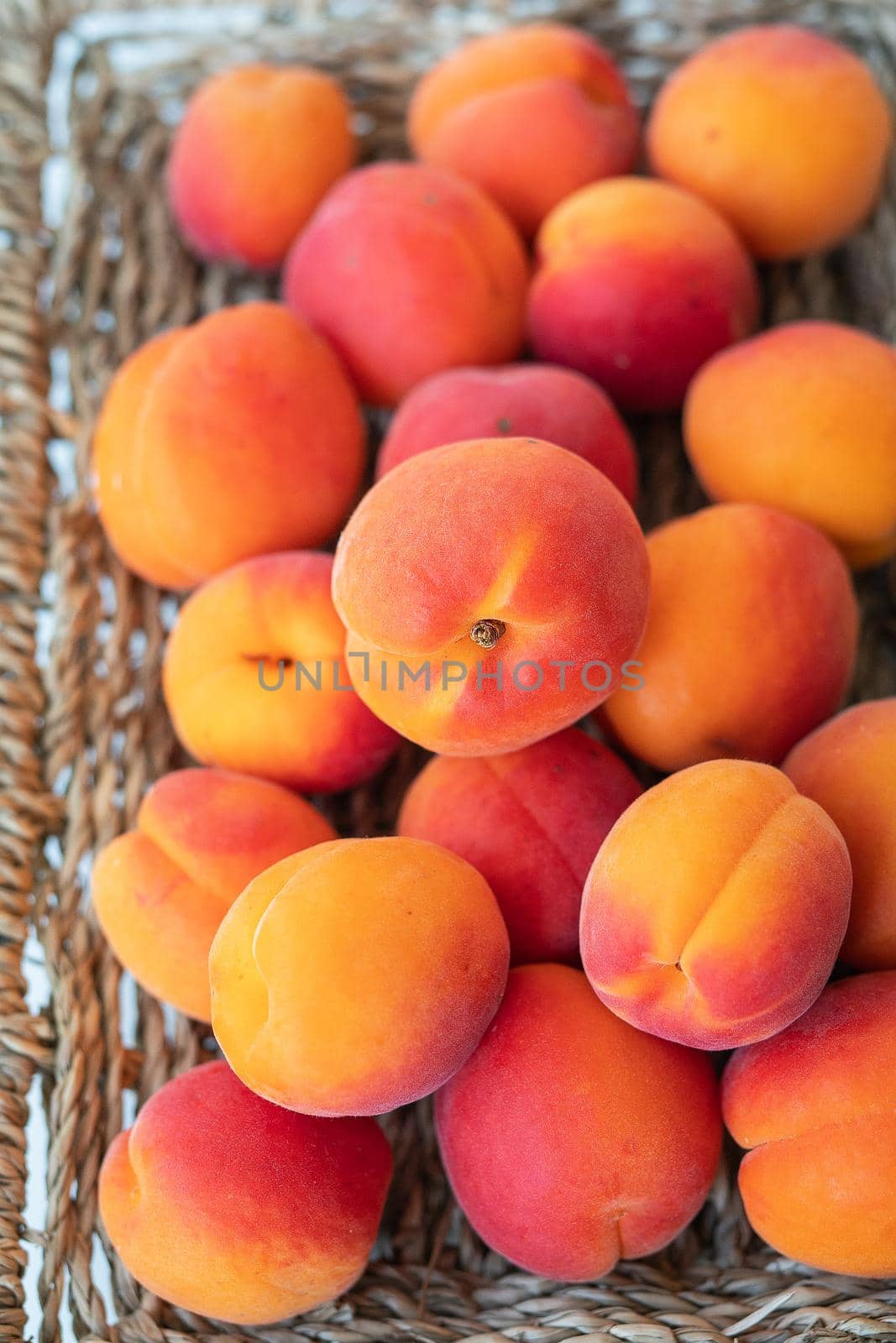 A large pile of ripe bright orange apricots lies close-up on a wicker plate