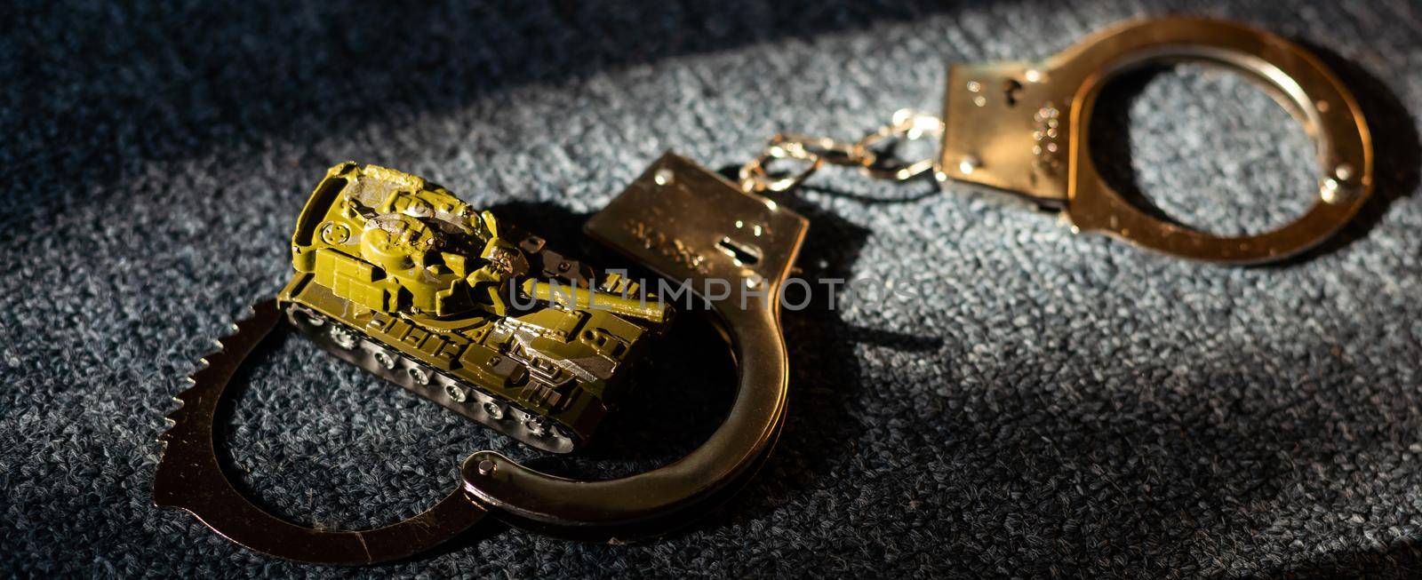 toy tank and handcuffs on a dark background.