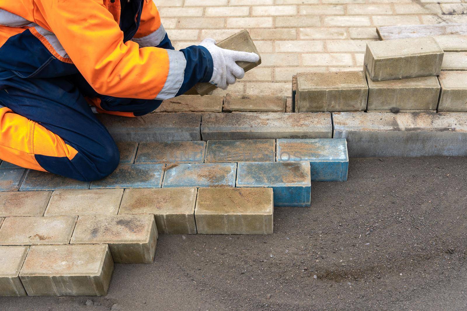 a worker in a protective work suit lays paving slabs. A professional master in work gloves lays paving stones. Paving of the site. Laying paving slabs in the yard of the house on a sandy foundation