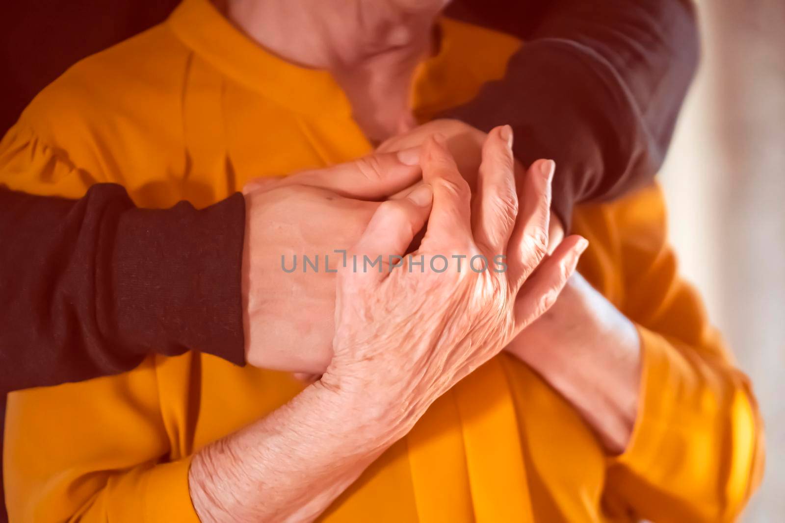 A young man, a volunteer, a son carefully hugs his beloved grandmother, supports and helps an elderly woman in retirement, his grandparent. Young male and female elderly hands with wrinkles closeup.