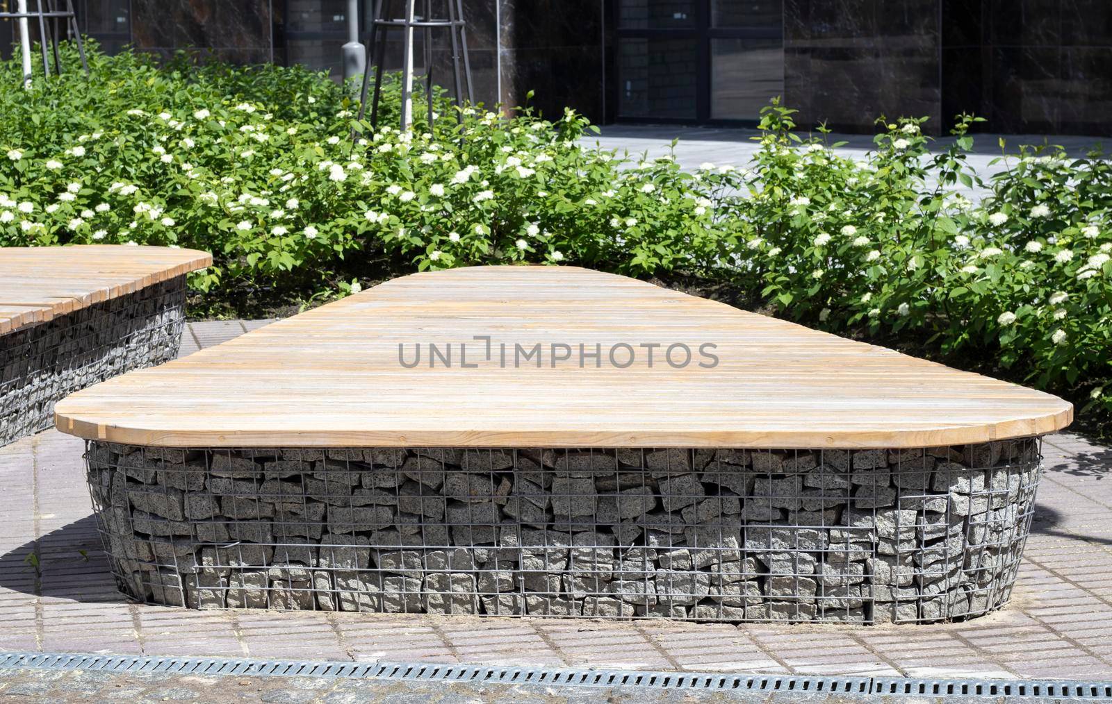 Wooden benches from gabion baskets with stones inside. Wood mounted on gabions. Benches of modern design. Detail of a low wood-topped gabion wall for use as a bench