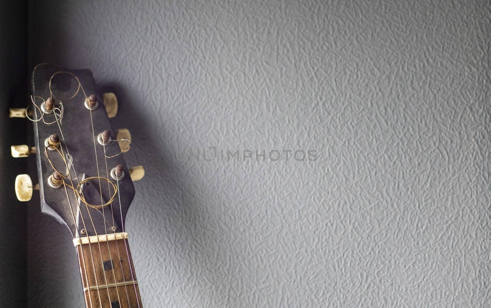 An acoustic old guitar in dust stands against a gray wall with copy space. Background for a screensaver with a musical instrument in the old style