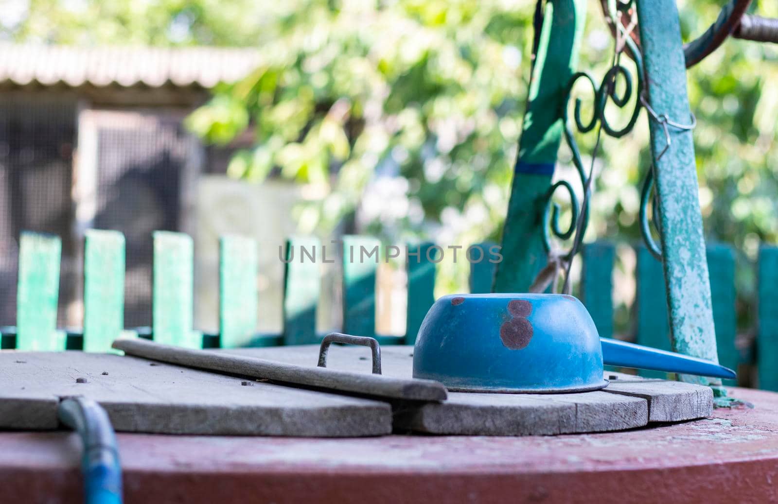 A well with a bucket in a European village. Sunny day. Metal bucket for a water well. Detail of a well with a tin bucket in the countryside. Decorating the garden with vintage items