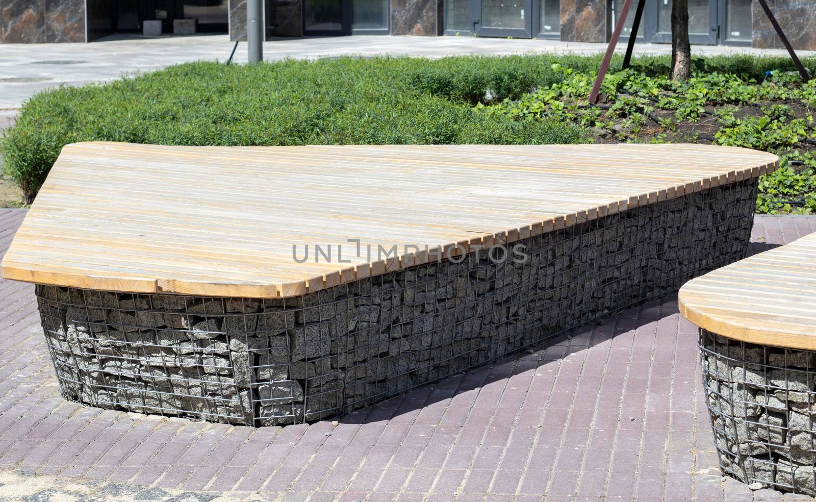 Wooden benches from gabion baskets with stones inside. Wood mounted on gabions. Benches of modern design. There is a recreation area. Detail of a low gabion wall with a wooden top