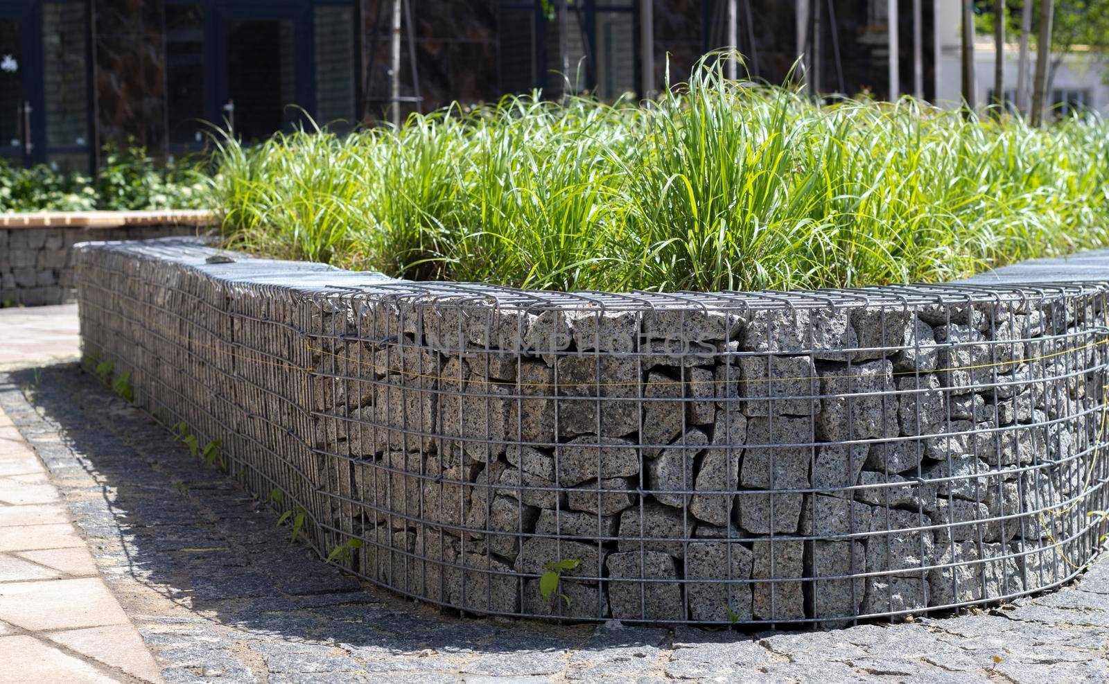 Basket support wall made of granite gabion. Gabions in the garden. Modern Gabion fence with stones in wire mesh. Gabion wire mesh fencing with natural stone and shrubs