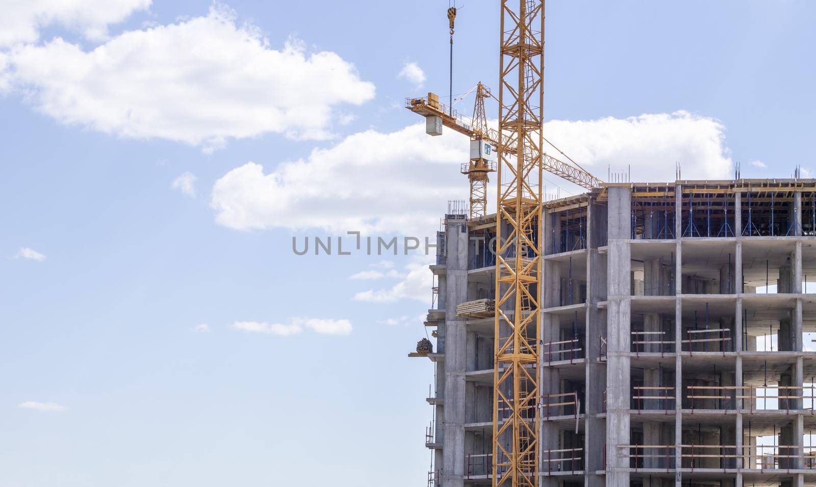 A working construction tower crane against a cloudy sky on a sunny day. The concept of urban development and construction. Industrial background. Crane engineering, construction industry tool