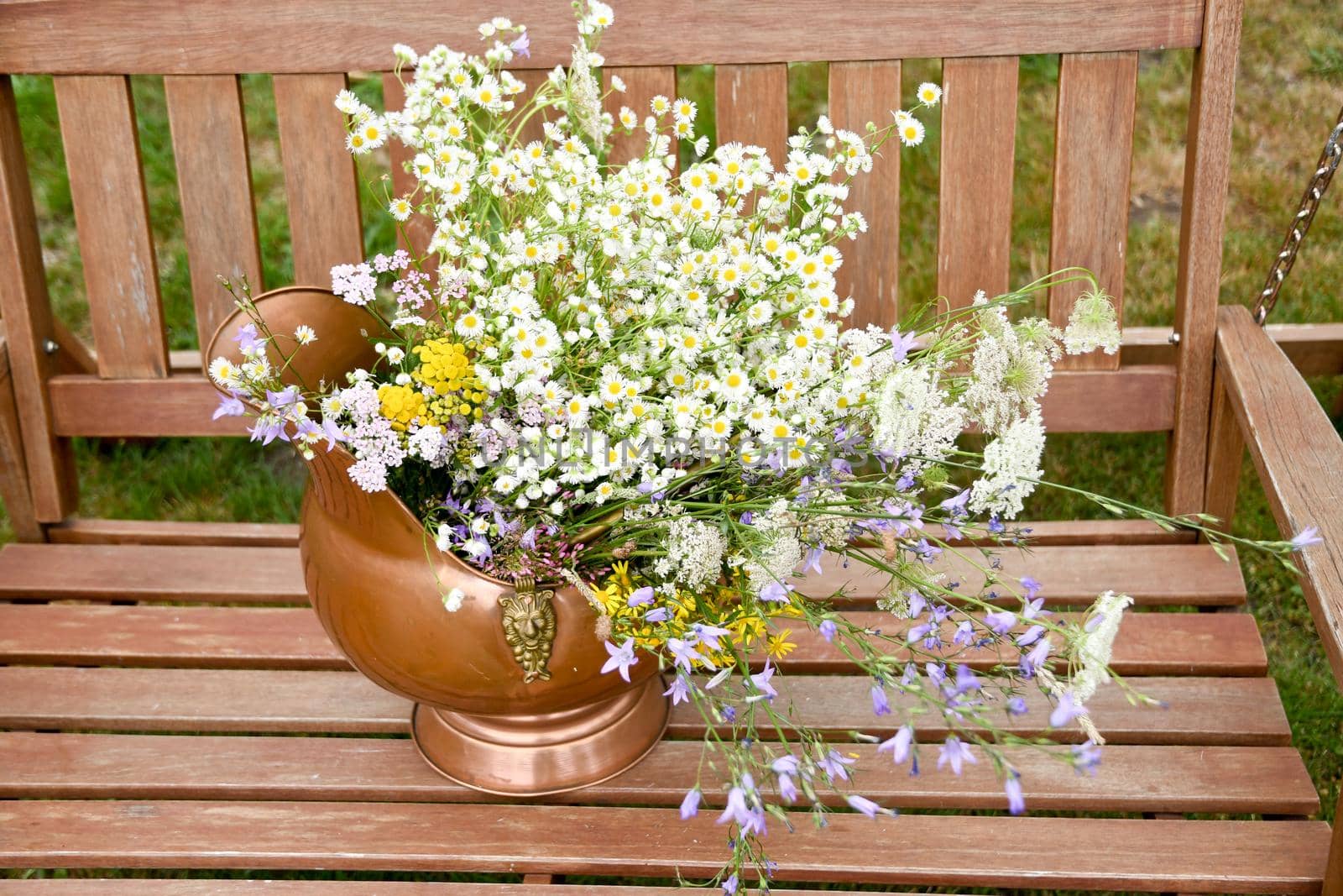 beautiful copper vintage pot with a large bouquet of summer wild flowers stands on a wooden swing in the garden natural flower background, summer. High quality photo