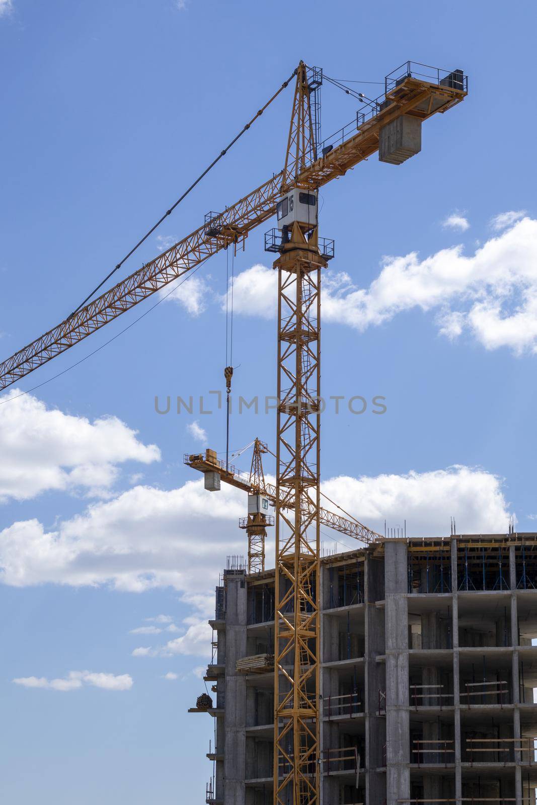 A working construction tower crane against a cloudy sky on a sunny day. The concept of urban development and construction. Industrial background. Crane engineering, construction industry tool