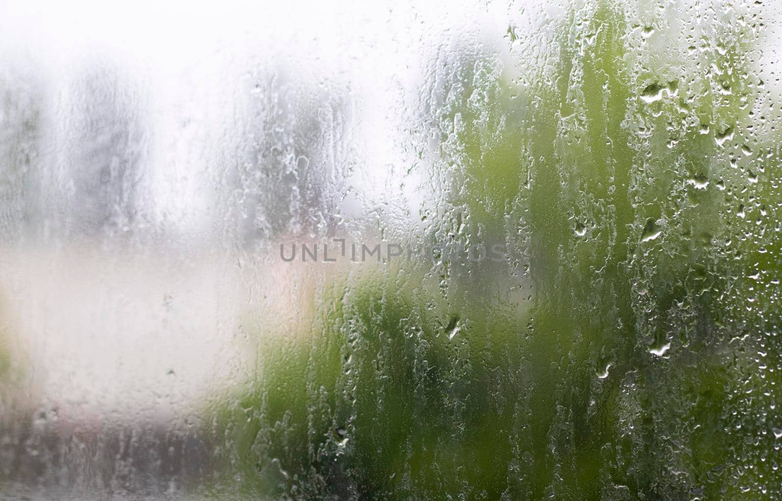 Heavy rain. Raindrops on the window glass on a summer day. Selective focus, shallow depth of field. Drops of water fall on a wet window. Glass full of drops during a downpour