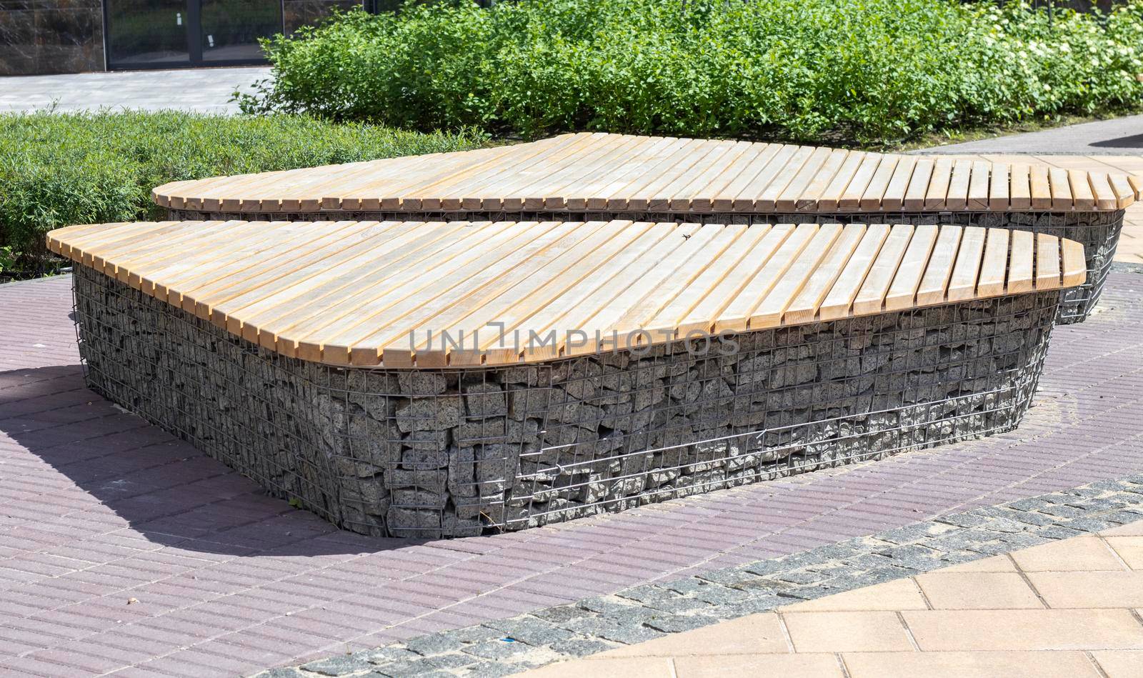 Wooden benches from gabion baskets with stones inside. Wood mounted on gabions. Benches of modern design. There is a recreation area. Detail of a low gabion wall with a wooden top