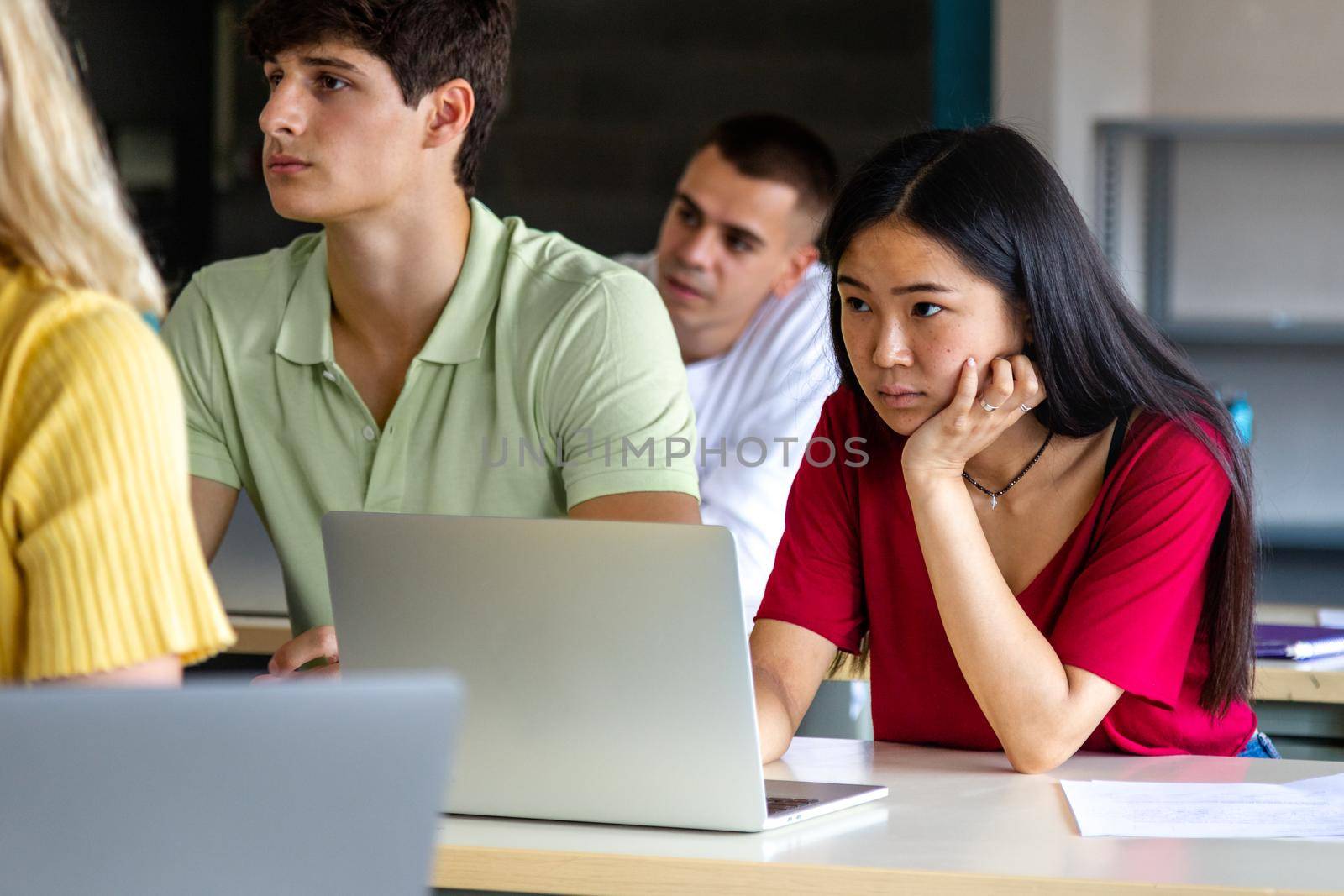 Asian female teen college student in class listening to lecture using laptop to take notes. by Hoverstock