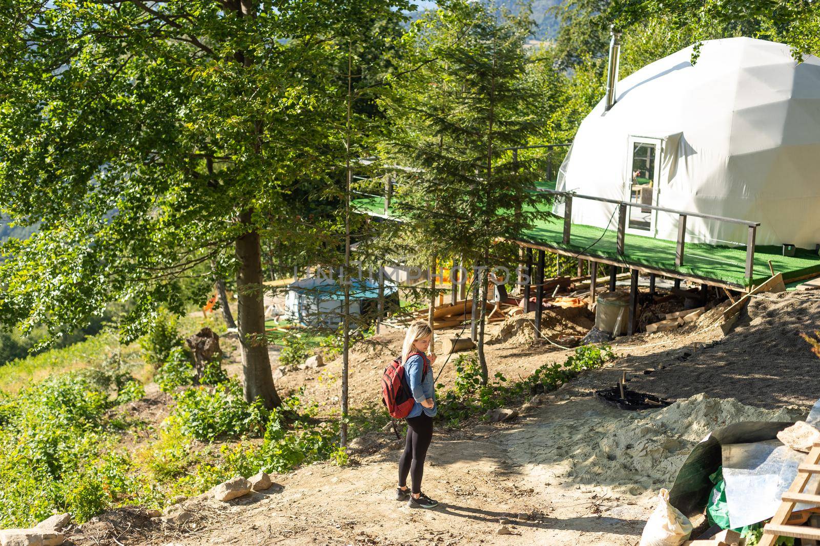 woman looking at nature geo dome tents. Green, blue, orange background. Cozy, camping, glamping, holiday, vacation lifestyle concept. Scenic outdoors cabin.