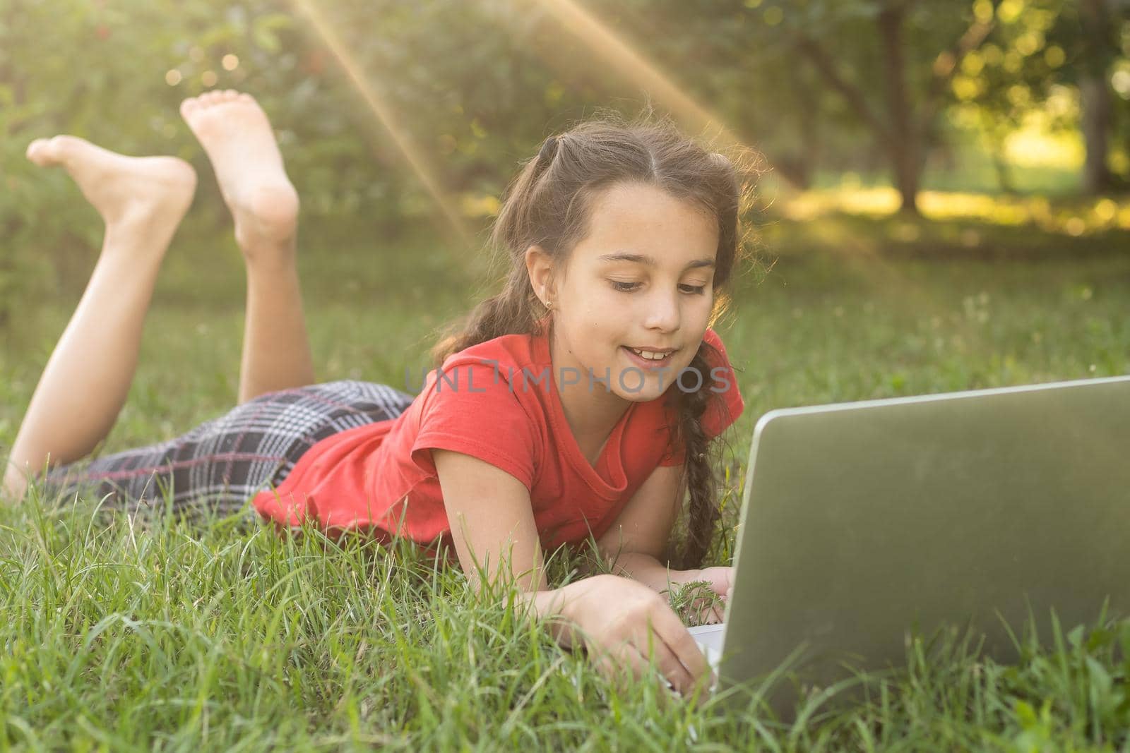 little girl usng laptop in a summer garden.