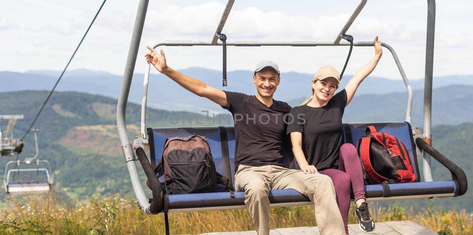 Man and a woman riding on the lift down the scenic Mountain during summer. Green tree forest surrounds the escalator. by Andelov13