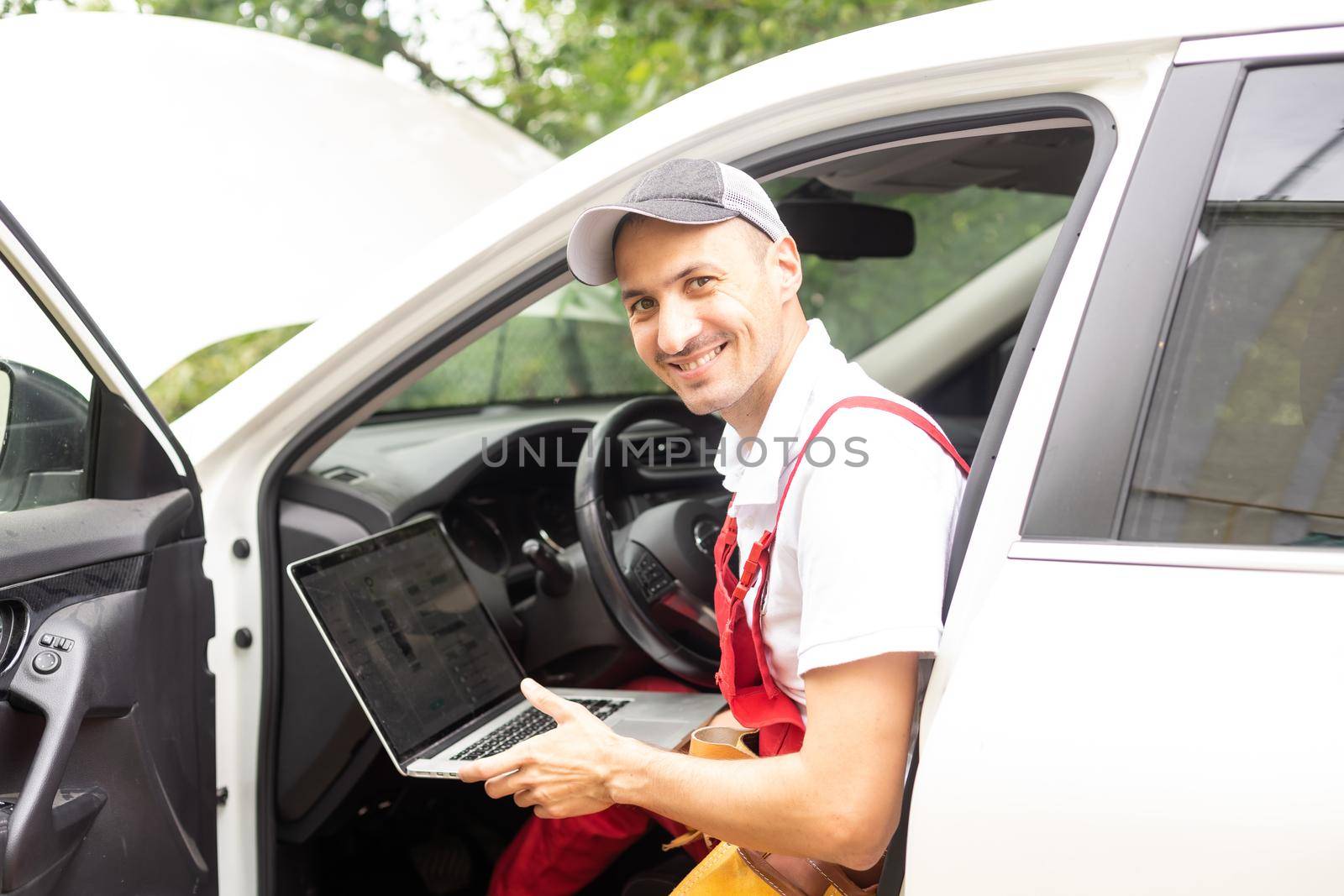 Mechanic with laptop near car engine. Modern car diagnostic program on screen. Car service concept by Andelov13
