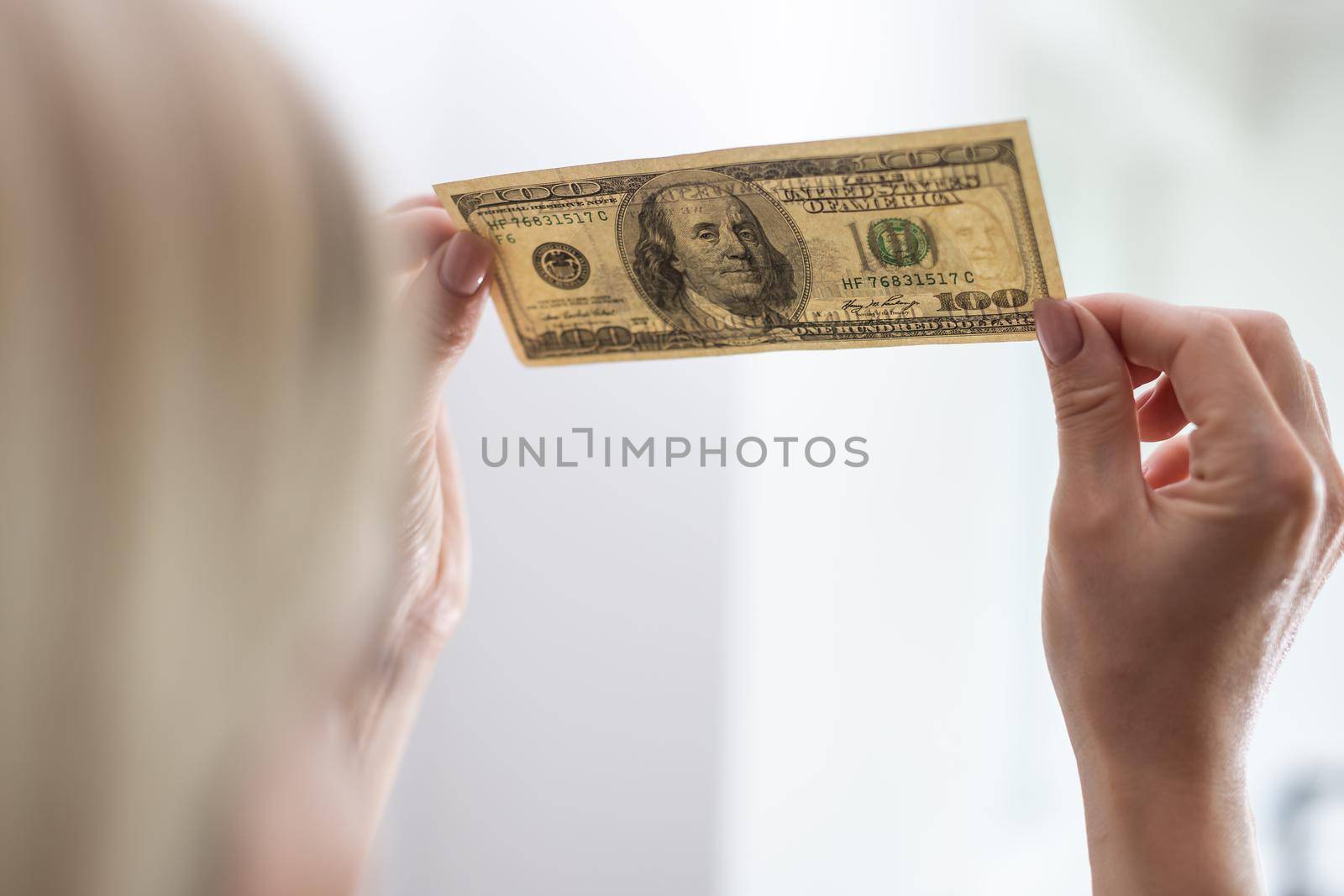 Woman holding dollar bill and looking at it with watermarks closeup. by Andelov13