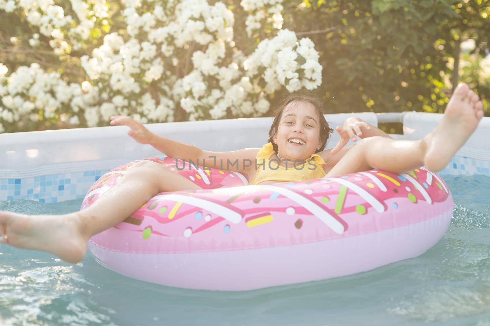 Happy little girl playing with colorful inflatable ring in outdoor swimming pool on hot summer day. Kids learn to swim. Child water toys. Children play in tropical resort. Family beach vacation.