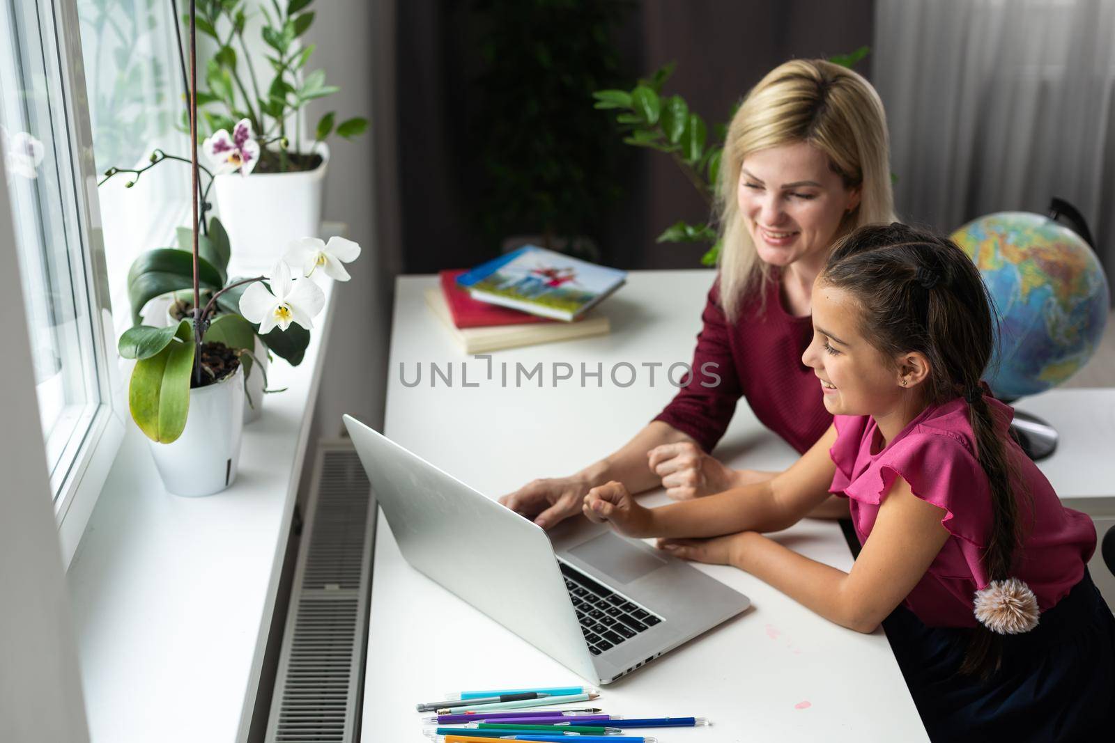 Beautiful young woman and her little cute daughter are using laptop at home. Enjoying spending time together.