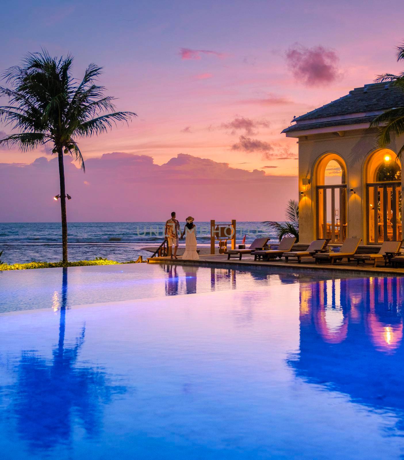 a young couple of men and women at a swimming pool during a vacation on a tropical island. man and woman in infinity pool during sunset. luxury vacation in Thailand pool of a luxury pool villa