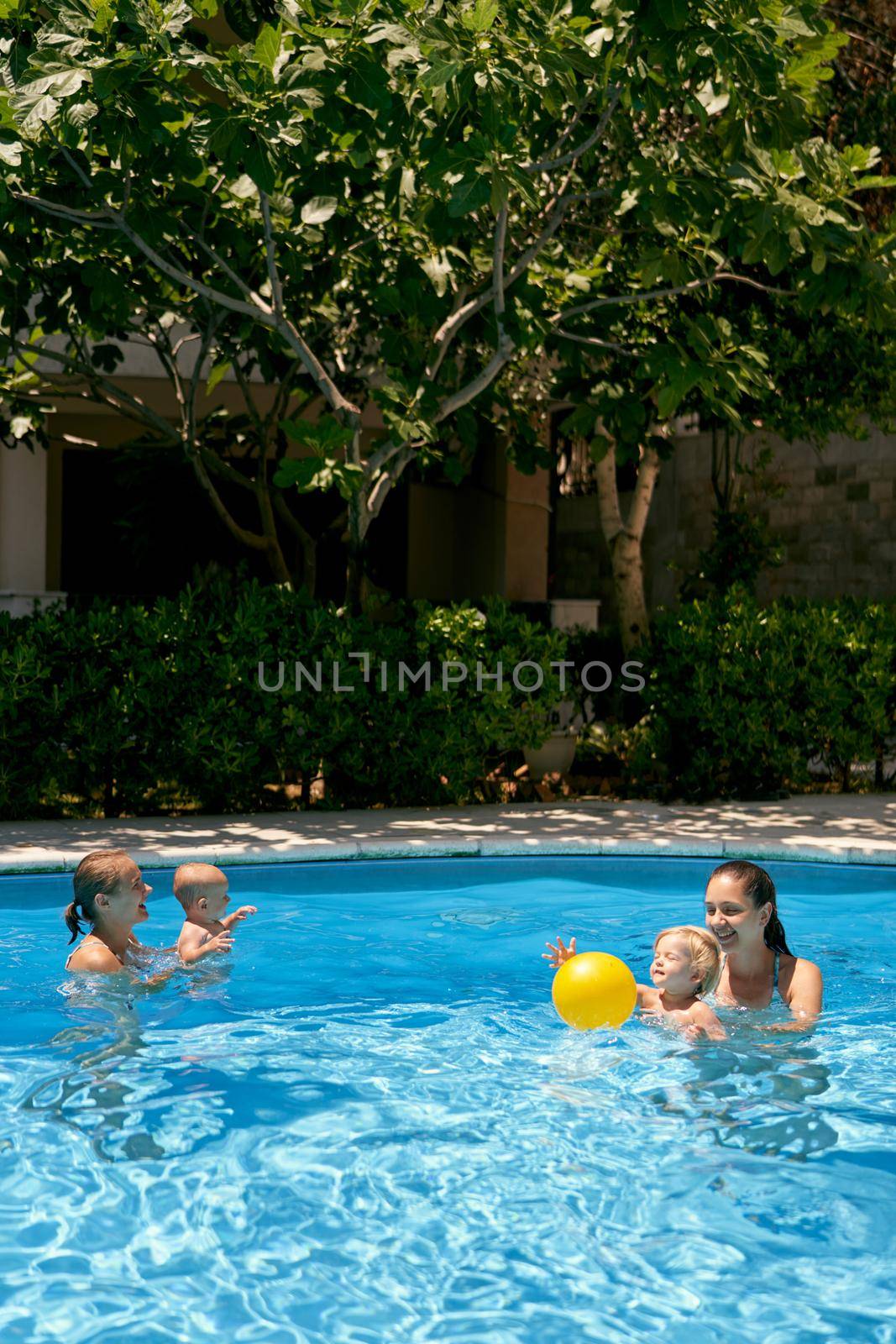 Moms with small children play with a yellow ball in the pool. High quality photo