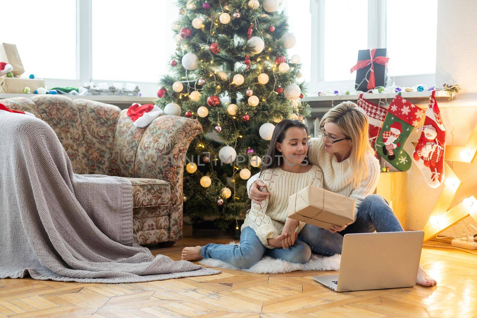 cheerful teenage girl and mother celebrating christmas at home and communicating online by Andelov13