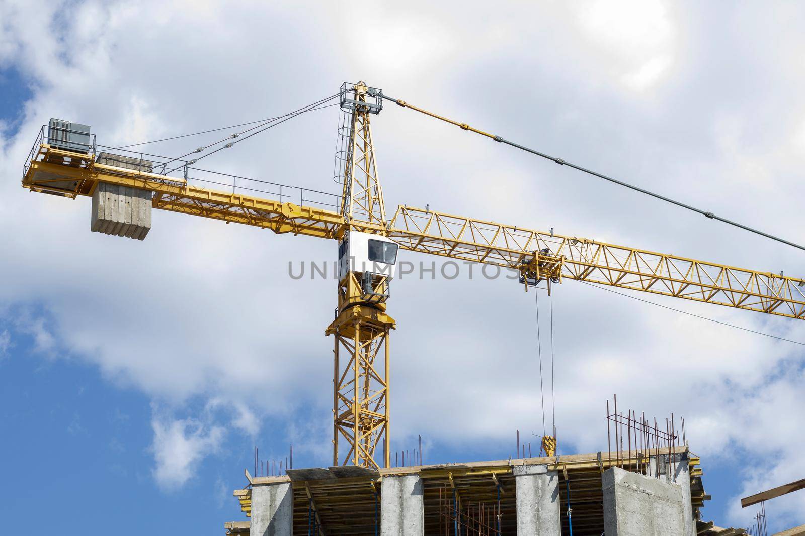 A working construction tower crane against a cloudy sky on a sunny day. The concept of urban development and construction. Industrial background. Crane engineering, construction industry tool