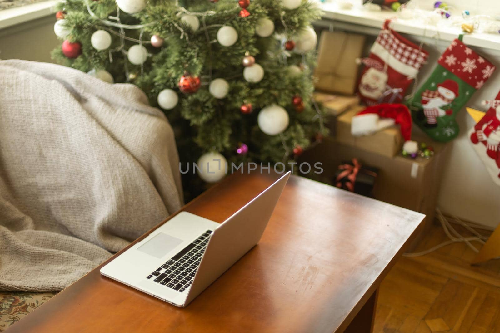 Laptop with empty screen on wooden table, blur Christmas tree and gifts on background. by Andelov13
