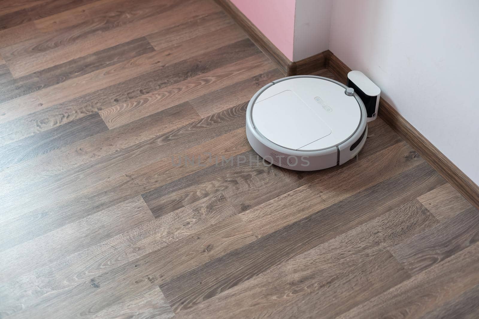 Robotic vacuum cleaner on laminate wood floor charging from base station. Smart cleaning technology. robot vacuum cleaner return to charging at dock in clean room floor.