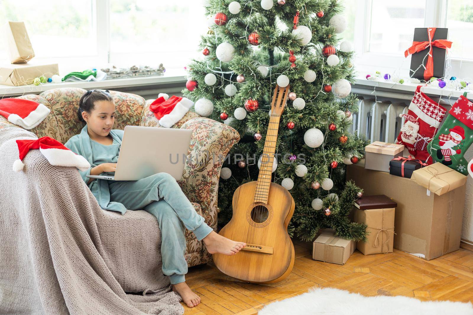 winter holidays, technology and children concept - little student girl with laptop computer at home over christmas tree background