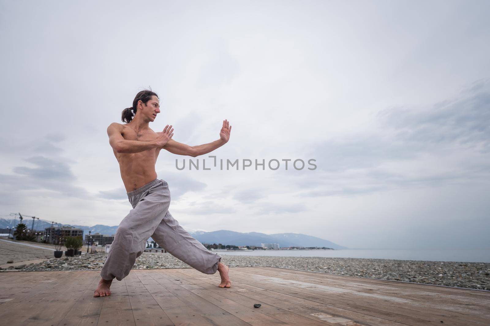 Caucasian man with naked torso practicing wushu on the seashore