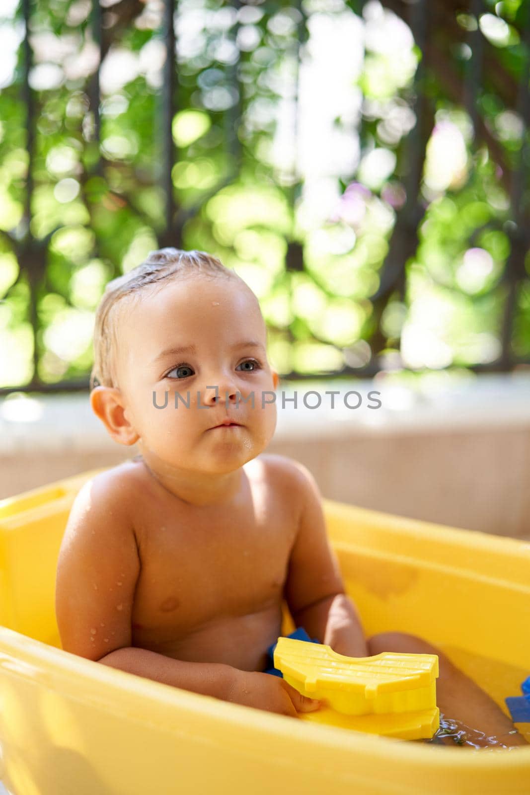 Little girl sitting in a bowl of water on the balcony. High quality photo