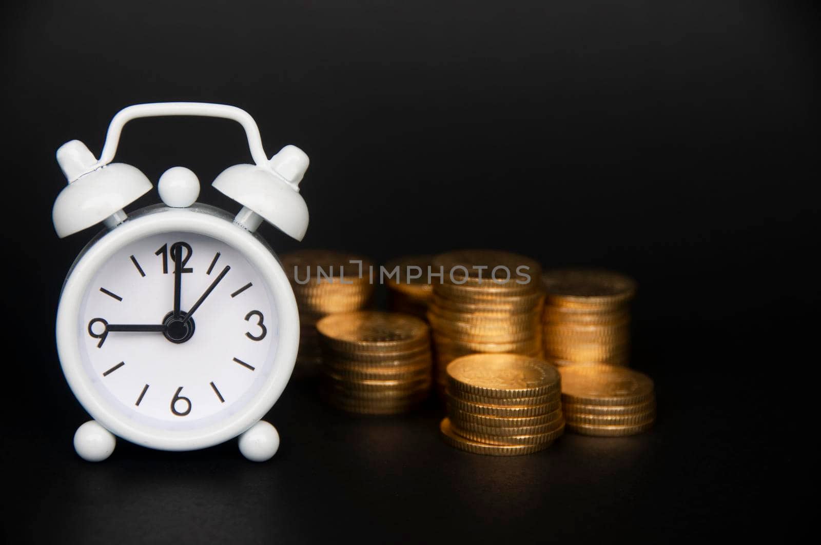 White alarm clock with gold coins isolated on dark background. Copy space and business concept.