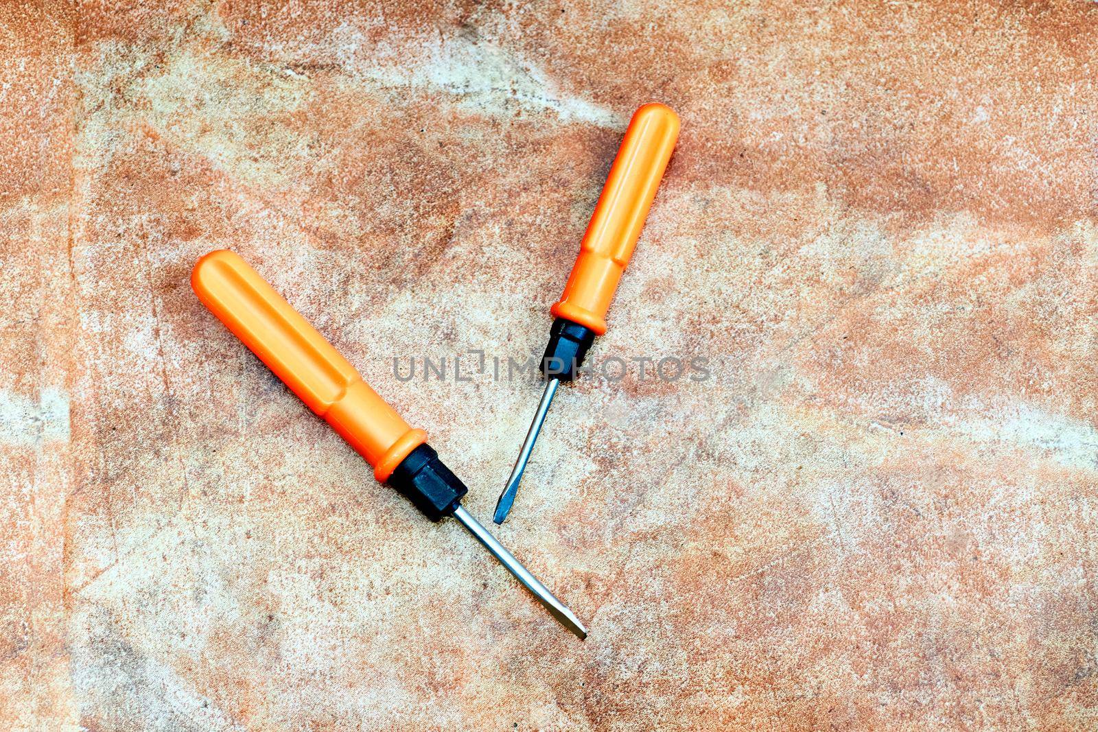 Two orange screwdrivers on brown marble tiles by jovani68