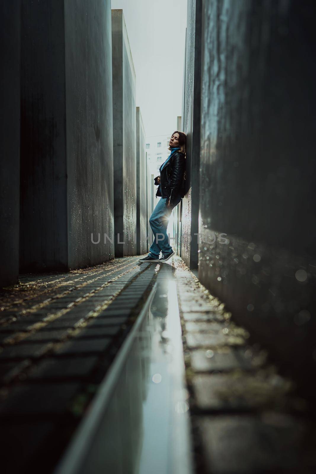 May 2022 - Berlin, Germany. Woman stands in dark maze between tall blocks in Holocaust Jewish Memorial of Murdered Jews. Light at the end of tunnel. High quality photo